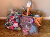 Wooden basket and fabric bag containing yarn and knitting needles placed on hardwood floor.