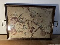 Front view of antique serving tray showing wooden frame, fabric with floral and bird design, and metal handles.