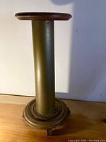Whole view of antique wood pedestal stand with metal column and round wooden base and top, shown standing upright.
