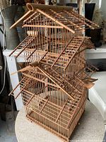 Full view of the large wooden birdcage showing the multi-level roof design with extending perches and vertical wooden bars forming the cage walls.