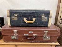 Two stacked vintage suitcases, smaller black crocodile embossed on top and larger brown below.