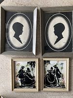 Two silver-toned framed black paper silhouette portraits of children, oval shaped with double line borders on cream backgrounds, approximate size 6x8 inches.