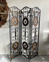 Full view of the metal room divider showing all three ornate panels, each with bronze medallions and leaf decorations.