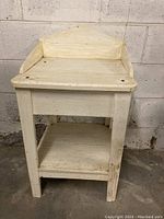 Front view of the painted wooden side table showing the triangular backboard, top surface, and lower shelf with the item's wear and paint condition visible.