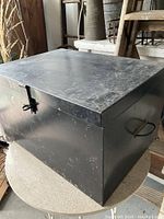 Photo of the black metal trunk showing the top and front with latch lock and side handle.