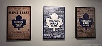 Three framed vinyl print artworks of Toronto Maple Leafs mounted on a white wall, each showing the blue maple leaf logo and various text details regarding the team.