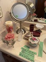 Photo of the full lot on bathroom countertop including True Glow light-up mirror, pink rose candle and stand, perfume bottle, floral container, and other small bowls and cups.
