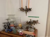 Wide view of various candle holders and candles arranged on a wooden surface underneath wall-mounted brass candle holders.