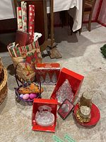 Full lot showing wrapping paper rolls, baskets with decorations, boxed Christmas tree decorations and snow globe, and gold glitter candles with decorative holder.