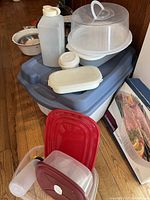 View of the lot with large blue Rubbermaid tote topped with assorted plastic food storage containers including a white rectangular container, a white pitcher, and a clear cake container with handle.