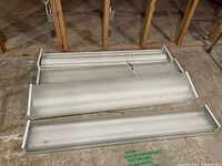 Four fluorescent light fixtures laid out on floor, two sizes visible, one missing diffuser cover