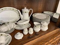 Full display of the Green Dale China set showing stacked plates, cups on saucers, teapot, cream and sugar bowl, gravy boat, salt and pepper shakers, serving platter and bowl with matching green floral border pattern on white china.