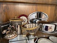 Wide view of the full lot showing various silver plated and metal dining accessories, a commemorative plate, and a decorative glass jar.