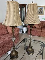 Full view of both brass table lamps with beige and gold striped fabric shades on glass coffee table.