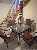 Square glass tabletop and base of set with four chairs and folded umbrella leaning against stair