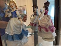 Blue dressed porcelain figurine holding a bluebird, detailed skirt and base, reflection shows second figurine