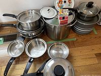 Multiple stainless steel pots stacked and displayed showing varying sizes and black handles, two pots with glass lids.