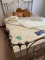 Full view of bed with mattress, comforter, and decorative pillows revealing metal frame design and bedding set.