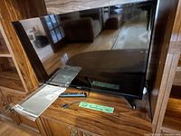 Front view of the 31-inch Samsung LED TV on wooden cabinet with remote and manual