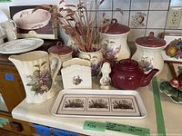 Full view of vintage floral ceramic kitchenware including canisters, milk bag holder, napkin holder, teapot, tray, and salt shaker.