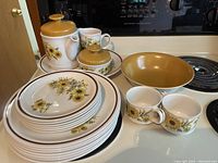 Full set of Daisy pattern dinnerware displayed on stove top featuring plates, bowls, cups, teapot, creamer, sugar bowl, and serving bowl