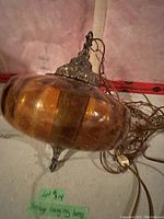 Vintage hanging lamp with orange/amber ribbed glass and metal fixtures lying on a concrete floor alongside a tangled hanging chain and power cord.