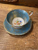 Cup and saucer together showing the overall blue and gold floral design and colorful floral center