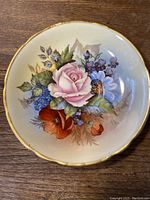 Top view of the hand-painted floral design on the saucer, showing pink rose, red poppy, blue and purple flowers, and green leaves with artist signature.