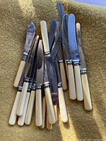 Photo of vintage cutlery spread on a yellow textile background, showing mostly knives with ivory-colored handles and metal blades.