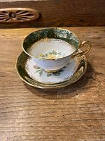 Cup and saucer set angled to show the cup handle, floral design inside the cup, and gold patterned rim.