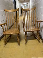 Set of two oak wood rocking chairs shown side by side in a hallway, showing full chair bodies including armrests and wooden rockers.