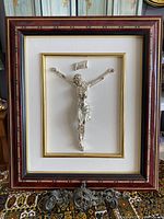 Silver crucifix with INRI plaque mounted in detailed wood frame with gold trim and inlay background, front view.