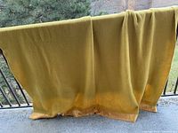 Gold wool blanket with silk trim displayed on railing outdoors. Shows full length and color.