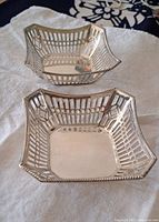 Pair of square antique silver dishes with lattice openwork sides and beaded edges, placed on white cloth.