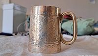 Angled side view showing detailed floral engraving on sterling silver stein and handle.