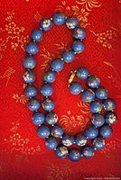 Full view of the vintage cloisonne necklace laid out on red patterned fabric showing blue enamel floral beads knotted on the strand.