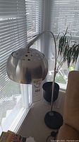Full view of arc floor lamp showing metal dome shade, curved arm, weighted base, and cord with foot switch.