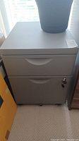 Full view of closed grey metal 2-drawer file cabinet with wheels and a cup on top.
