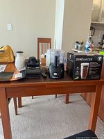 Kitchen appliances including Hamilton Beach food processor, Braun juicer, electric mixer, and ZeroWater pitcher in box on wood table in kitchen.