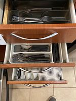 Top drawer containing black handled stainless steel forks and spoons, and a silver hand-hammered spoon visible at the top