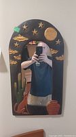 Full frontal view of carved wood framed mirror showing moon, stars, clouds, cactus, coyote, and pot design.