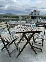 Full patio set on balcony featuring one table and two folding chairs with wood slats and weathered finish.
