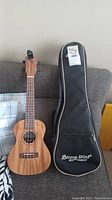Full view of the Strongwind ukulele with its black soft carrying case placed on a couch.