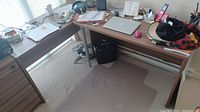 Full view of the L-shaped wood desk in a room, shows surface, legs, and surroundings