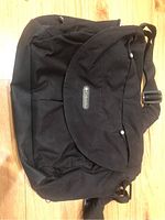 Front view of black Columbia diaper bag with flap closed and adjustable shoulder strap visible