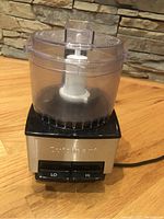 Front view of Cuisinart food processor showing stainless steel base, clear plastic bowl and two speed buttons LO and HI