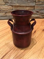 Front angled view of the red rustic metal vase showing handles and flared top edge.