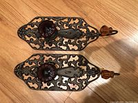 Two decorative wall hooks laid on wood floor showing full length and design detail.