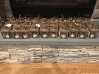 Front view of 25 identical gold mini lanterns arranged in rows on a stone ledge, showing the exterior design and size.