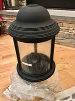 Photo showing the black metal light fixture with seeded glass panels, decorative rope detail on the dome top, designed for outdoor post mounting.